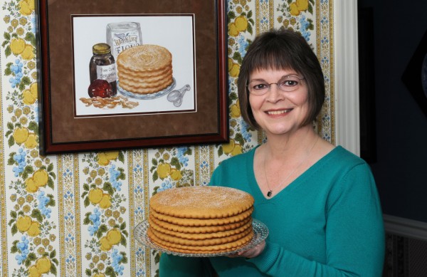 Jill Sauceman with her traditional dried apple stack cake. She inherited the recipe from her grandmother, Nevada Parker Derting, who lived in Scott County, Virginia. The watercolor painting of the stack cake on the wall was done by Nancy Jane Earnest.