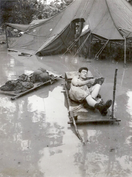 A soldier enjoys a paperback in a flooded camp. 