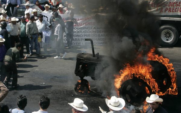Mexican farmers protesting the removal of import tariffs on U.S. and Canada agricultural goods—as agreed to under the North American Free Trade Agreement (NAFTA)—gather around a tractor set on fire by demonstrators during a protest in Mexico City, Jan. 31, 2008. Photo by Eduardo Verdugo/Associated Press.