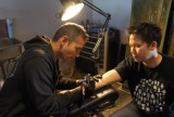 Ky-Phong Tran getting a tattoo with his right arm out while a tattoo artist leans in.