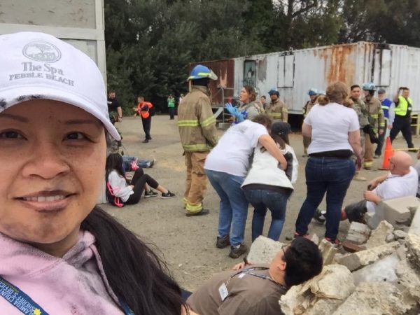 Jenny takes a selfie while other volunteers act out a disaster drill in the background. 