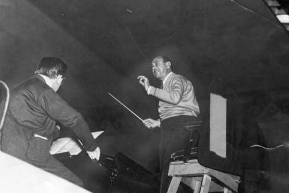 Black and white photo of Arnold Schoenberg conducting during a rehearsal with the LA Philharmonic Orchestra in 1935.