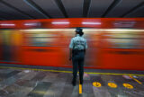 A member of the Mexican National Guard stands in front of a red moving train in the Mexico City Metro subway.