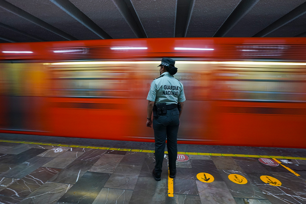 A member of the Mexican National Guard stands in front of a red moving train in the Mexico City Metro subway.