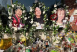 An altar to the victims of the Monterey Park shooting. Flowers, candles, small pictuers, and notes fill the table. Above the altar are three larger photos of three different victims, framed with flowers.