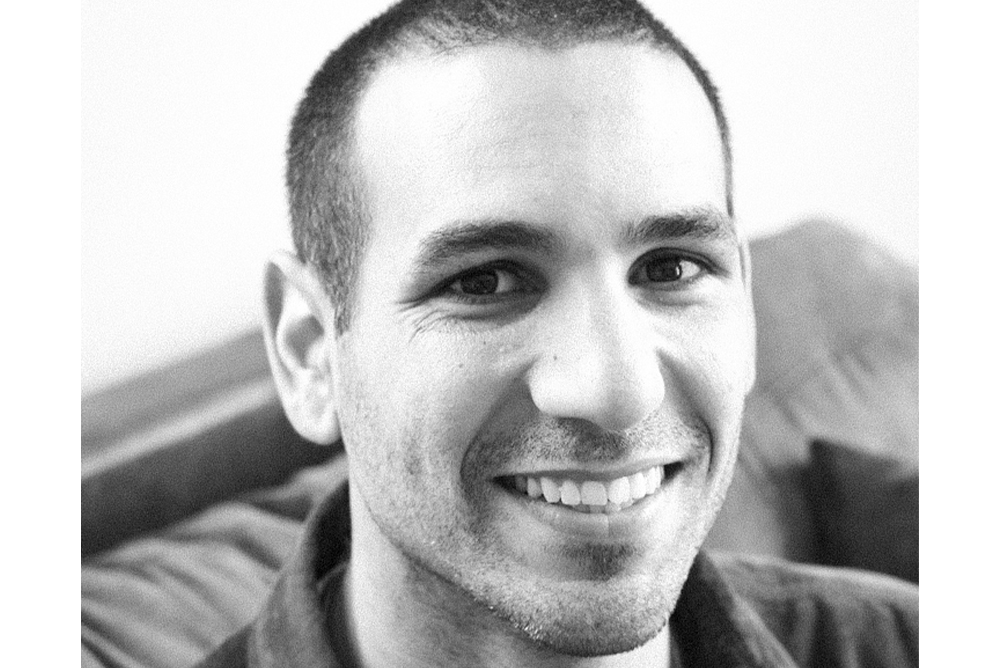 Black and white close up of Andrew Calis facing the camera with a grin.